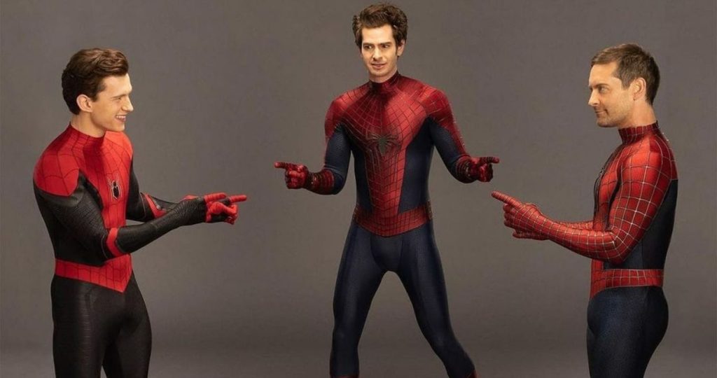 Tom Holland, Andrew Garfield, and Tobey Maguire dressed as Spider-Man pointing at each other in a humorous pose, recreating the famous Spider-Man pointing meme.