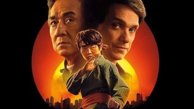 "Poster for Karate Kid Legends featuring Jackie Chan, Ralph Macchio, and Ben Wang. Chan and Macchio stand in the background with serious expressions, while Wang, in a martial arts stance, is in the foreground. The sunset-lit skyline of New York City is seen at the bottom, with a red-orange sun creating a dramatic backdrop.