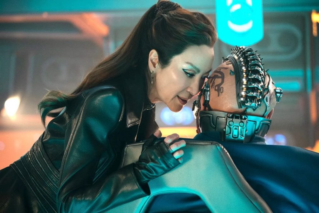 "Michelle Yeoh as Emperor Philippa Georgiou in dark attire, whispering to a tech-augmented character."