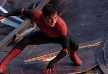 Tom Holland dressed as Spider-Man crouching in a defensive stance. His red and black suit contrasts against the metallic debris in the background, suggesting a battle scene.