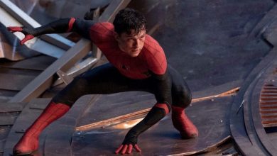 Tom Holland dressed as Spider-Man crouching in a defensive stance. His red and black suit contrasts against the metallic debris in the background, suggesting a battle scene.