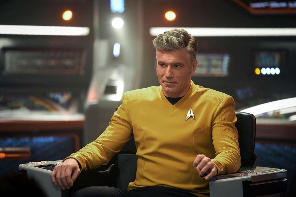 "Captain Pike, portrayed by Anson Mount, sits confidently in his command chair aboard the USS Enterprise, wearing his signature yellow uniform."